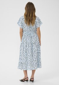 Ljusblå klänning med ett blommönster, korta ärmar, elastisk midja och midi-längd, som matchas med svarta slingback-skor.
