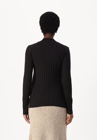 Maglietta nera a maniche lunghe con scollo alto, dal design aderente e dalla texture morbida, abbinata a una gonna beige texturizzata.