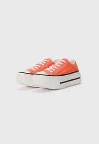 Red canvas sneakers with white laces, rubber toe caps, and platform soles featuring a black stripe. Rounded shape, textured soles for grip.