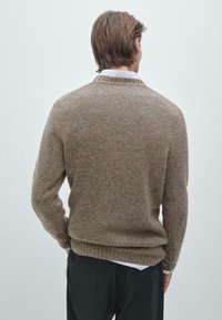 Brauner Wollpullover mit strukturiertem Strickmuster, geripptem Saum und Rundhalsausschnitt, über einem weißen Hemd getragen, von hinten betrachtet.