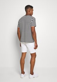 T-shirt sa crno-belim prugicama s kratkim rukavima, uparen s bijelim trapericama. Outfit je upotpunjen bijelim sportskim cipelama.