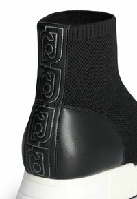 Stivaletto alla caviglia in maglia nera con tacco in pelle nera liscia e suola in gomma bianca. Presenta dettagli del logo tono su tono sul lato per un design aggiuntivo.