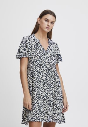 Robe à manches courtes en crème avec un motif abstrait bleu marine, décolleté en V et silhouette fluide. Tissu léger avec une coupe décontractée.