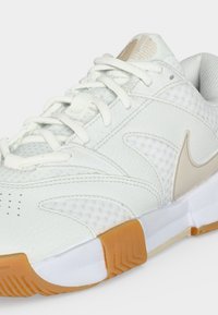 Λευκό αθλητικό παπούτσι με μπεζ λογότυπο Nike, λευκά κορδόνια, πανί και δερμάτινο επάνω μέρος και λευκή σόλα με καφέ ελαστικές λεπτομέρειες.