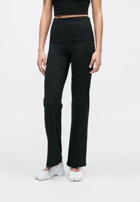 Μαύρο, εφαρμοστό παντελόνι με ψηλή μέση, μαλακή υφή και σχέδιο με φουσκωτά μπατζάκια, σε συνδυασμό με λευκά αθλητικά παπούτσια.