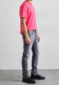 Růžové bavlněné tričko v kombinaci se šedými slim-fit džíny a černými teniskami. Tričko má kulatý výstřih a džíny mají mírné opotřebení.