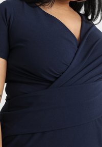 Mörkblå klänning med en insvept design, korta ärmar, mjukt tyg och samlad detaljer vid midjan för en figursydd look.