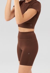 Brązowy sportowy crop top i szorty z wysokim stanem wykonane z gładkiego materiału. Cechy to krótkie rękawy i małe logo na końcu.
