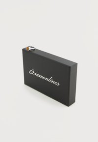 Anillo de plata con piedra de ámbar descansando sobre una caja de joyería negra de Commonlines sobre fondo blanco.