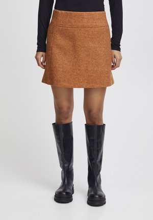 Jupe courte évasée en mélange de laine, couleur orange brûlé, avec une texture lisse, présentant des coutures latérales et associée à des bottes en cuir noir jusqu'aux genoux.