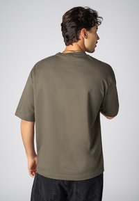 Olive green short-sleeve t-shirt with a relaxed fit, round neckline, and smooth fabric texture. Features stitch detailing and dropped shoulders.