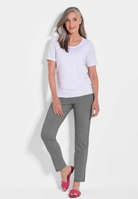 Haut blanc à manches courtes, pantalon à carreaux noir et blanc, et sandales en toile roses. Le mannequin se pose les mains sur les hanches.