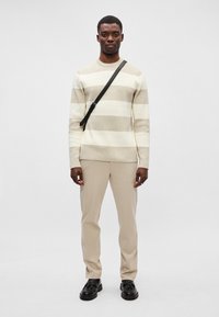 Kermainen ja harmaa raidallinen neule, jossa on ribbitekstuuri, yhdistettynä beigeihin housuihin. Musta olkahihna ja kengät täydentävät asukokonaisuutta.