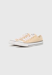 Lys ferskenfargede kanvas-sneakers med hvite snørebånd, gulløyer, teksturert tåhette, svartstripet mellomsole, klassisk lavt design.