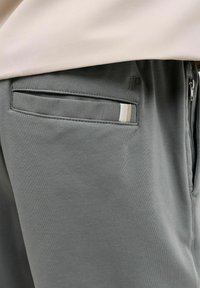 Graue Sporthosen verfügen über eine hintere Tasche mit einem kontrastierenden gestreiften Akzent. Die Stoffstruktur wirkt glatt und leicht.