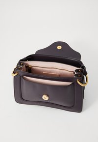Sac à main en cuir violet avec quincaillerie dorée, une poche extérieure et un intérieur rose clair avec un compartiment zippé.