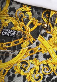 Versace Jeans Couture denim har ett grått leopardtryck med utsmyckade gula barockmönster, guldfärgad metall och en framträdande varumärkesskylt.