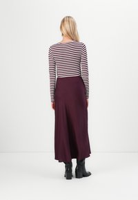 Prugasta bluza z dolgimi rokavi v beli in globoko burgundski barvi, v kombinaciji z airy burgundskimi maksi krili. Dopolnjena z črnimi čevlji na peto.