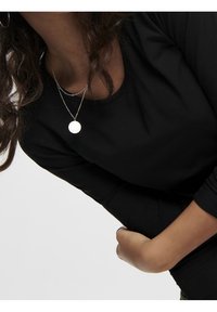 Svart långärmad tröja med rund halsringning, bärs med lager av silverhalsband som har en cirkulär berlock och en delikat kedja.