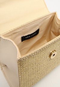 Borsa a tracolla beige intrecciata con una parte anteriore texturizzata, hardware dorato e un'etichetta nera cucita. Interno foderato in tessuto beige, con ampio spazio aperto.