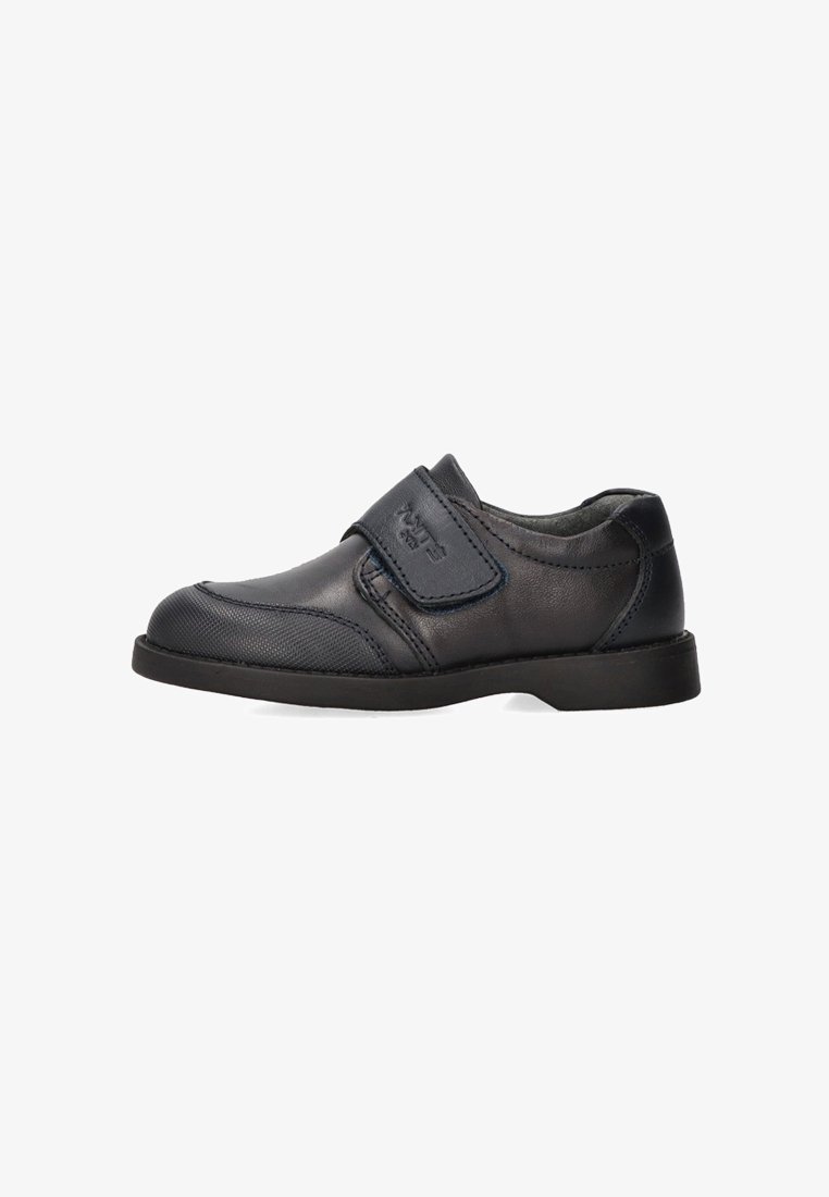 Zapato de cuero negro con una correa de velcro, punta redonda, superficie texturizada y suela baja de goma. Adecuado para un uso casual o formal.