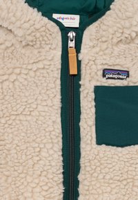 Giacca in pile color crema con zip verde sul davanti, dotata di tasca a toppa e zip di contrasto. Morbida al tatto.