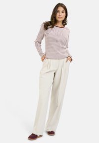 Striped long-sleeve top in burgundy and white, paired with cream high-waisted trousers. Model wearing maroon slip-on shoes.