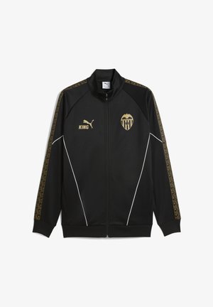 Sort zip-up jakke med guld accenter, der har et logo og ordet "KING" i guld. Sidepanelet har geometriske mønstre. Hvid piping-detalje.
