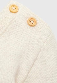 Kermanvärinen neulepaita, jossa on tekstuuri ja kaksi puunappia olkapäällä. Pehmeä kangas, joka on rentoa mitoitusta.