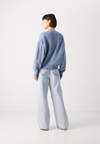 Light blue knitted sweater with a relaxed fit paired with wide-leg light blue jeans. Soft texture, round neckline, and minimal detailing.