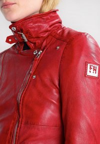 Red leather motorcycle jacket featuring a high collar, zip closure, snap buttons, and a patch with "FN" logo on the sleeve.