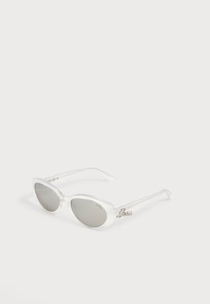 Lunettes de soleil œil de chat avec montures transparentes claires et verres teintés gris, avec un logo métallique "Guess" sur la branche.