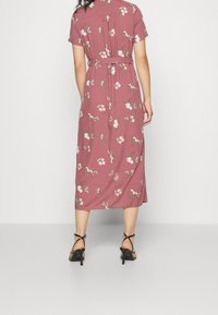 Różowa midi sukienka w kwiaty z krótkimi rękawami, z wcięciem w talii i paskiem do związania; zdobiona małymi białymi i zielonymi wzorami kwiatowymi.