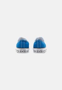 Sneaker di tela blu con design a bassa punta, suola in gomma bianca e logo nero "CONVERSE ALL STAR" sul tallone. Accenti di cuciture bianche.