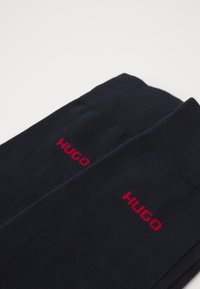 Marineblaue Socken aus weichem Material mit auffälligem roten "HUGO"-Logo. Schlichtes Design mit geripptem Bund.