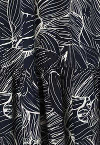 Tissu foncé avec un motif abstrait de feuille blanche, comportant des sections froncées créant des plis texturés et du volume.