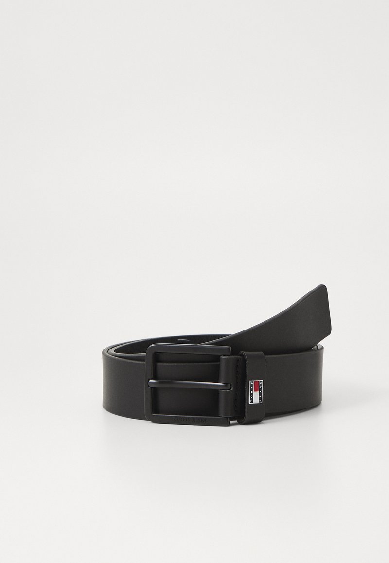 Zwarte leren riem met een matte afwerking, rechthoekige zilveren gesp en een klein logo label met rood, wit en blauwe accenten op de lus.