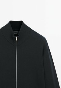 Schwarze Zip-Jacke aus Baumwollmischung, mit geripptem Kragen und glatter Textur, ausgestattet mit einem silbernen Reißverschluss vorne.