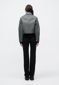 Sivá skrátená bunda z textúrovaného materiálu so štruktúrovaným golierom, skombinovaná s čiernymi nohavicami a robustnou čiernou obuvou.