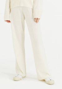 Crème-kleurige wijde broek gemaakt van zachte stof, met verticale naden en een comfortabele pasvorm, gecombineerd met witte sneakers.
