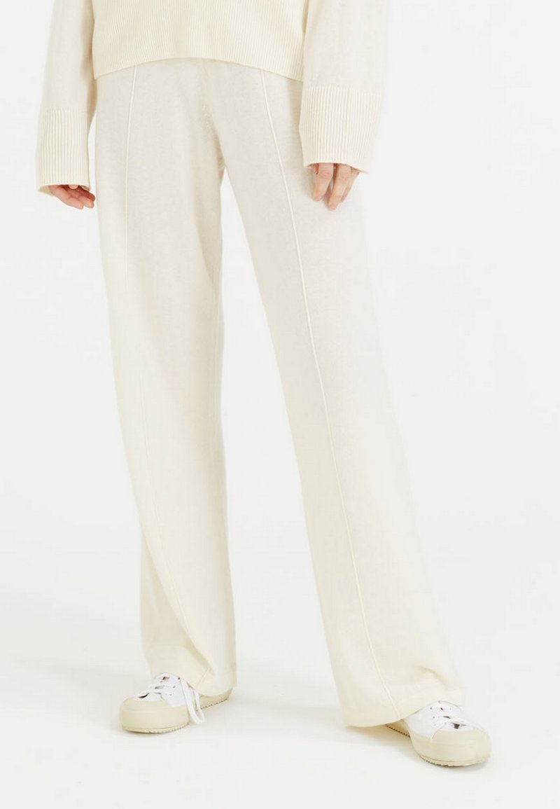 Crème-kleurige wijde broek gemaakt van zachte stof, met verticale naden en een comfortabele pasvorm, gecombineerd met witte sneakers.