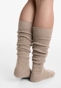 Knæhøje, ribbede sokker i en blød beige farve, der har et slouchy design og tekstureret stof.