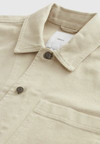 Camicia in corduroy beige con colletto a punta, chiusura con bottoni in metallo, taschino sul petto sinistro e superficie a coste testurizzata.