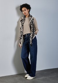 Beige žebrovaný top spárovaný s vysokým pasem tmavými džínami s širokými nohavicemi a černobílým šálkem s vzorem. Boty jsou béžové plátěné espadrilky.