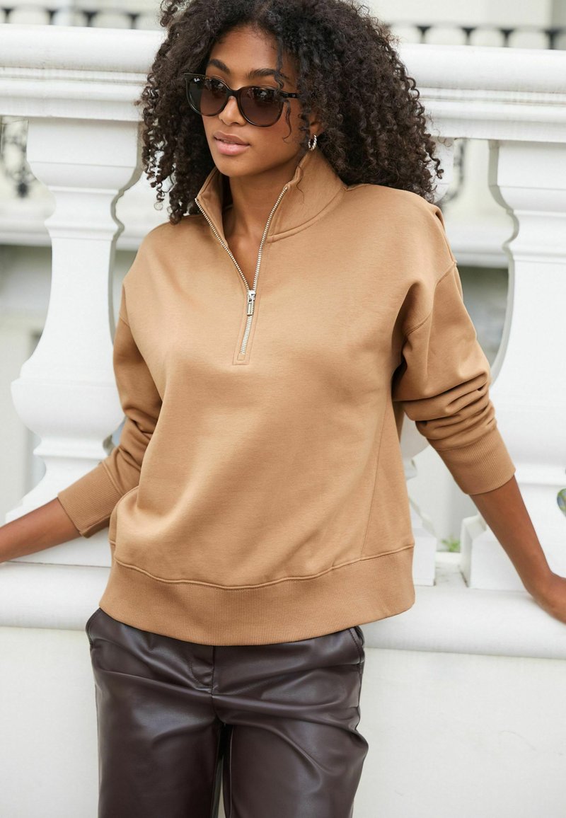 Tan met rits sweatshirt van zachte stof, met een hoge kraag en ribbelmanchetten, gecombineerd met bruin faux leren broeken.