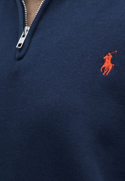 Tumesinise kudumusega pullover lukuga kraega. Ilma oranži tikkitud ratsutaja logota. Sile tekstuur ja vormis disain.