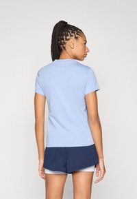 Ανοιχτό μπλε εφαρμοστό t-shirt με κοντά μανίκια, στρογγυλή λαιμόκοψη και διακριτική λεπτομέρεια λογοτύπου στο τελείωμα, σε συνδυασμό με σκούρο μπλε σορτς.