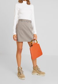 Mini gonna a scacchi, top bianco a maniche lunghe, stivali chunky color sabbia e una borsa arancione con manico in tartaruga.