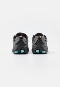 Graue Sportschuhe mit schwarzen Akzenten, versehen mit einem strukturierten Obermaterial, gepolstertem Kragen und türkisfarbenen Details an der Außensohle für zusätzlichen Grip.