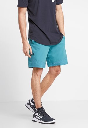 Turkusowe spodenki sportowe z siateczkowymi wstawkami, połączone z czarną koszulką i czarnymi sneakersami z białymi akcentami i paskami.